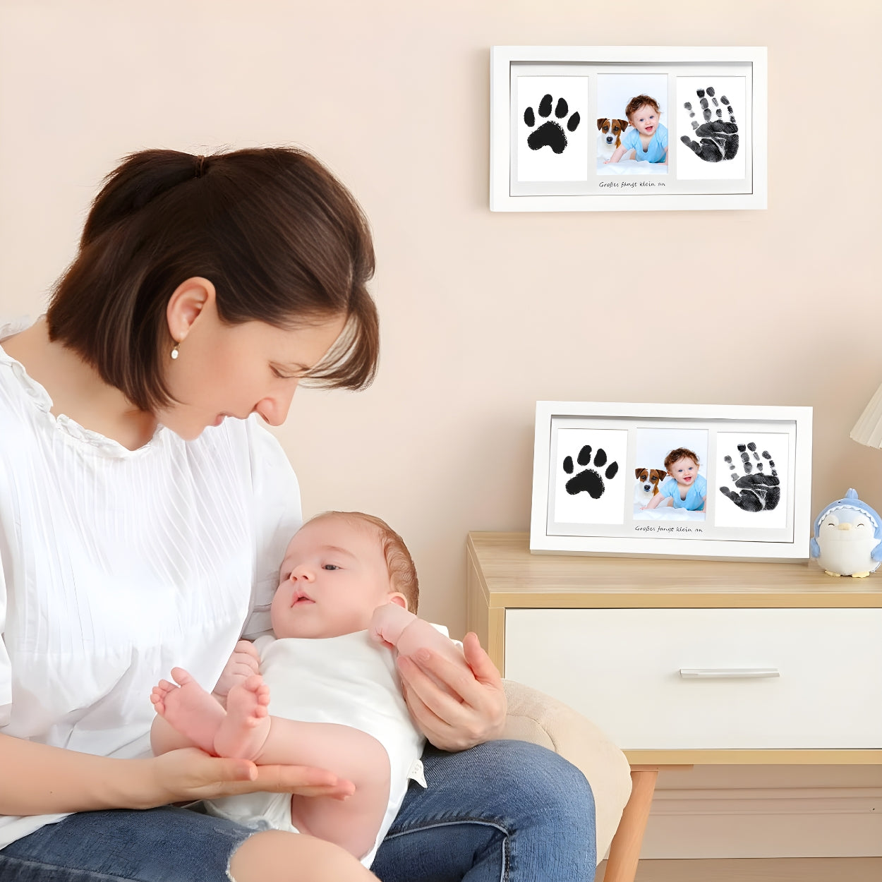 Woman holding a baby with two framed paw print and handprint photos on a wall and desk - Little Treasures